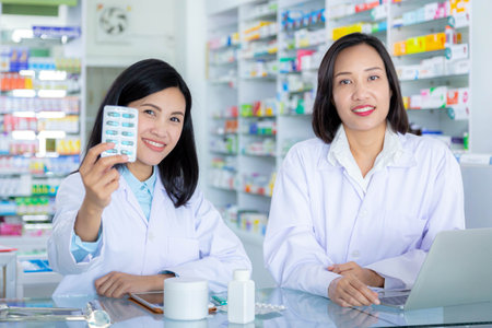 Smiling asian pharmacist holding capsules medicine in pharmacy with her colleague. Healthcare and medical concept.の写真素材