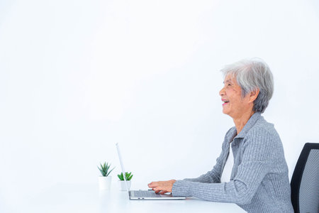 Happy old woman working on laptop computer at home office. Internet search, Online communication...
