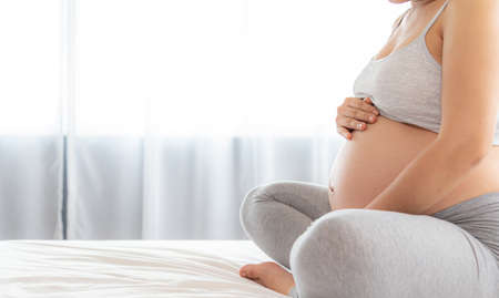 Pregnant woman holds hands on belly on bed. Pregnancy and people concept.の写真素材