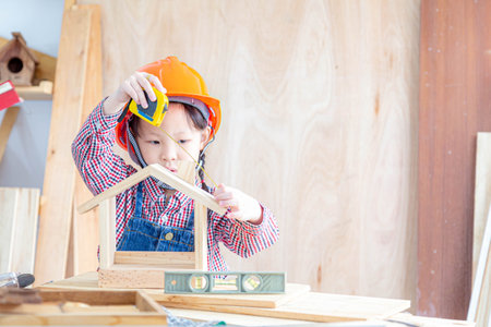 Asian little girl craftswoman measuring size of wooden house toy in carpentry shop.の写真素材