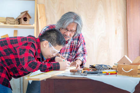 Asian senior carpenter man teaching asian boy craftswoman measuring size of wooden at carpentry shop. Family; carpentry; woodwork and kid concept.の写真素材