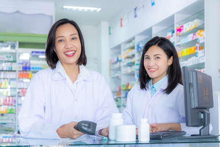 Two asian pharmacists working in a pharmacy drugstore. Health care and medical concept.Pharmacist scanning barcode of medicine drug in a pharmacy drugstore.の写真素材