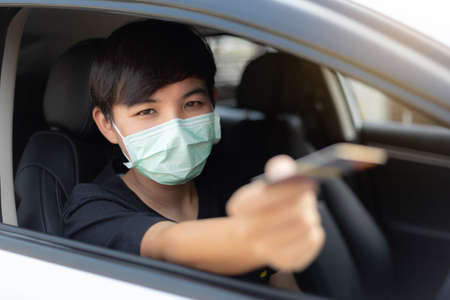A young man wearing protective mask used credit card for payment at drive thru food service. Outbreak COVID-19, Medical, Healthcare and Quarantine concept.の写真素材