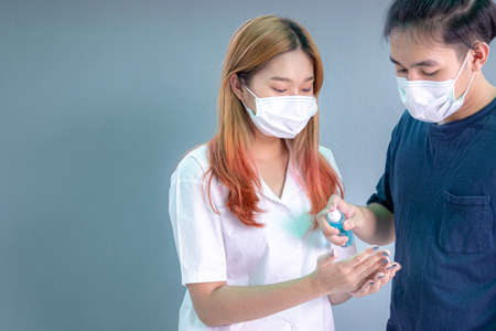 Young man  and women wear masks use alcohol spray or alcohol antiseptic gel to clean hands and prevent germs.の写真素材
