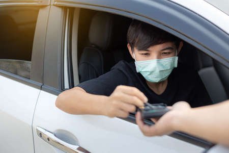 A young man wearing protective mask used credit card for payment at drive thru food service. Outbreak COVID-19, Medical, Healthcare and Quarantine concept.の写真素材