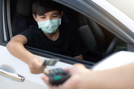 A young man wearing protective mask used credit card for payment at drive thru food service. Outbreak COVID-19, Medical, Healthcare and Quarantine concept.の写真素材