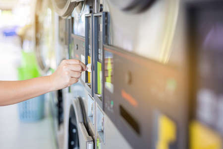 Hand woman putting coin in washing machine. Coin Washer and Dryer with integrated payment system.の写真素材