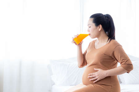 Asian pregnant woman drinking orange juice for good health. The concept of healthy food for pregnant women.の写真素材