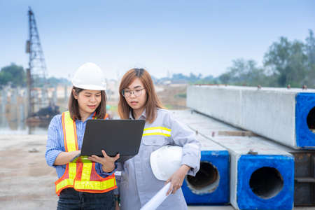 Two female architect leader working with laptop and blueprints at construction site or building site.の写真素材