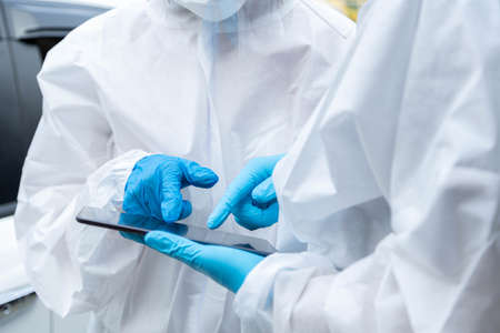 Close up of two doctor with PPE protective suit are using smartphone to check the outbreak information.の写真素材