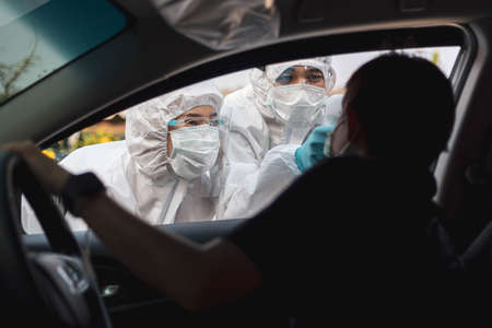 Medical staffs with PPE use infrared thermometer gun to check body temperature at drive thru station in hospital. New normal healthcare and medical concept.の写真素材