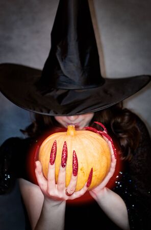 Pretty young witch with black hat, long nails and pumpkinの写真素材