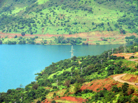 View of a scenic lake at a placed named Lavasa in India, surrounded by lush green mountains. Vehicles traveling on a road passing thru the hills get to experience amazing viewの写真素材