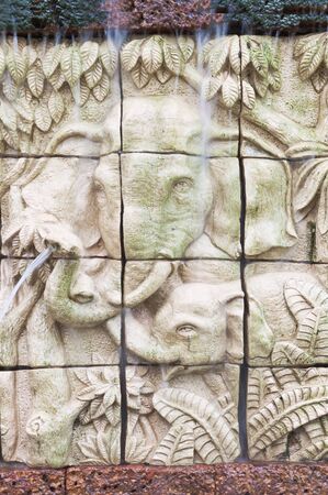 Elephants in low relief statue cut out as jig saw image and water fall in front of.の写真素材