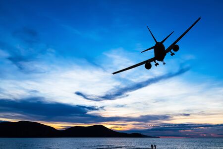 Silhouetted commercial airplane flying above the sea at sunsetの写真素材