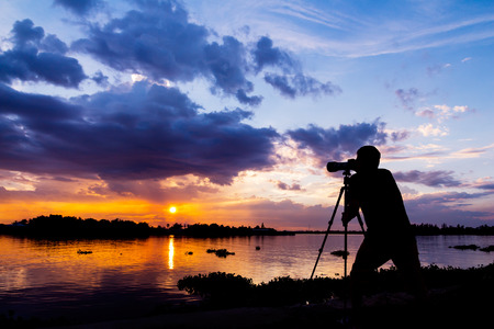 silhouette of photographer taking photo at sunset beside the riverの写真素材