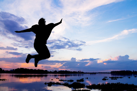 Silhouette lady jumping happy beside the river at sunsetの写真素材