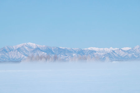 Winter landscape with snow-capped mountains and blue sky in the backgroundの写真素材