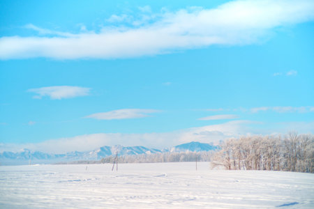 beautiful winter landscape with snow-covered field and blue sky with cloudsの写真素材