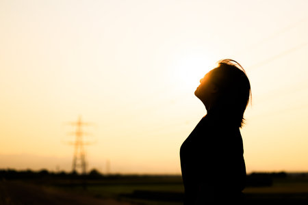 Silhouette of a beautiful young woman standing in the field at sunsetの写真素材
