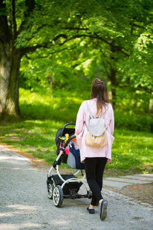 Happy mother walking with baby stroller in the parkの写真素材