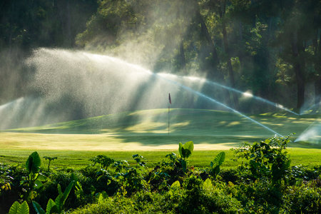 Golf course with water sprinkler in the morning, Thailand.の写真素材