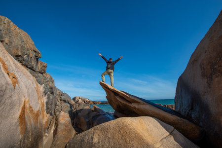 Young man standing on a rock by the sea and raising his hands up.の写真素材