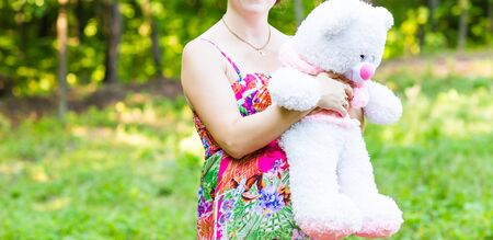 Toy bear cub against a stomach of the pregnant woman. The pregnant woman with a toy bear on a meadowの写真素材