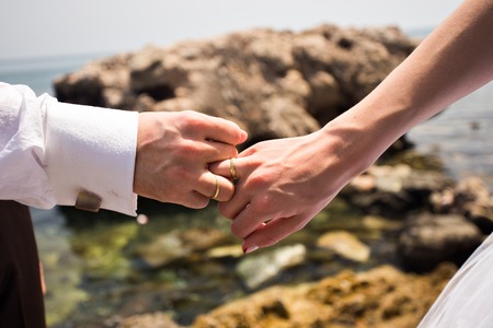 Holding Hands with wedding rings on the background of seaの写真素材
