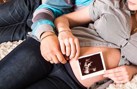 Young couple holding an ultrasound scan of their expecting baby at homeの写真素材