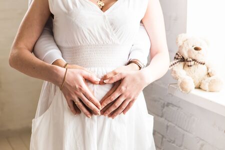 Pregnant Woman and Her Husband holding her hands in a heart shape on her baby bump.の写真素材