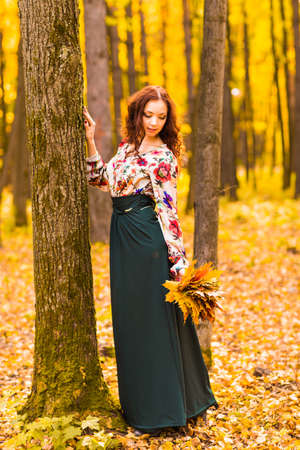Young woman with autumn leaves in hand and fall yellow maple garden backgroundの写真素材