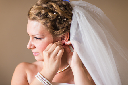 Beautiful bride in white wedding dress puts on earring.の写真素材