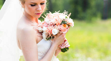 Beautiful bride with wedding bouquet of flowers outdoors in green parkの写真素材