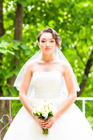 Beautiful bride girl in wedding dress with bouquet of flowers, outdoors portrait.の写真素材