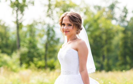 Beautiful bride girl in wedding dress  and bouquet of flowers, outdoors portrait.の写真素材