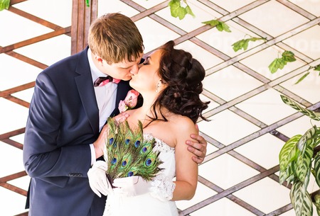 wedding couple kissing, bride holding fan of peacock feathers, the groom embracing her.の写真素材
