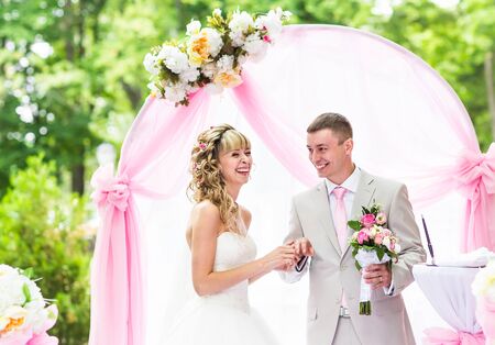Happy bride putting a ring on groom's finger during wedding ceremony.の写真素材
