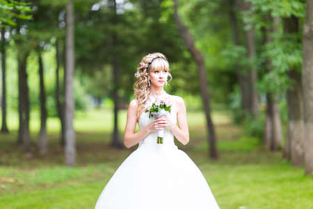 Beautiful bride with wedding bouquet of flowers outdoors in green parkの写真素材