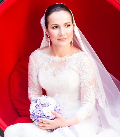 Young bride sitting in a red chair in the studioの写真素材