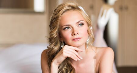 Beautiful young bride with wedding makeup and hairstyle in bedroom, attractive newlywed woman have final preparation for wedding. Happy Bride waiting groom. Marriage Wedding day moment. Bride portraitの写真素材