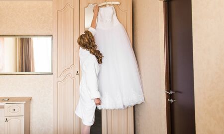 Beautiful young bride with wedding makeup and hairstyle in bedroom, attractive newlywed woman have final preparation for wedding. Happy Bride waiting groom. Marriage Wedding day moment. Bride portraitの写真素材