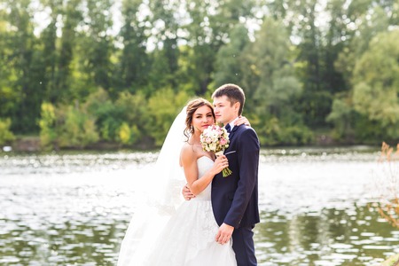 Wedding couple standing and hugging near lakeの写真素材