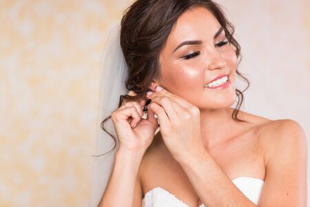 Elegant blonde bride putting on earrings closeup, preparing for wedding