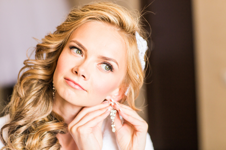 Elegant blonde bride putting on earrings closeup, preparing for wedding.の写真素材