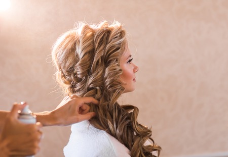 Wedding makeup artist making a make up for bride. Beautiful sexy model girl indoors. Beauty blonde woman with curly hair. Female portrait. Bridal morning of a cute lady. Close-up hands near faceの写真素材