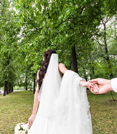 Beautiful young woman bride holds the hand of a man in outdoors. Follow me.の写真素材