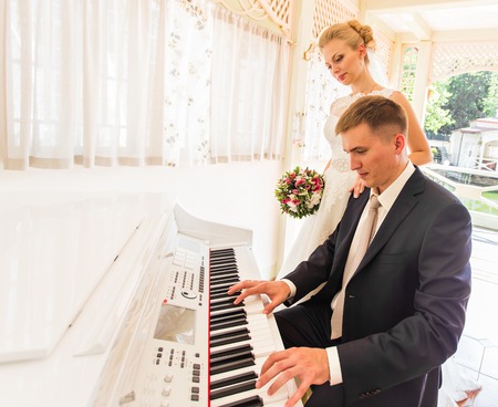 charming wedding couple playing on an old piano in the roomの写真素材