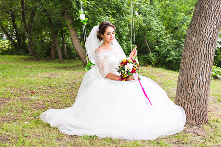 Portrait of a beautiful bride in white wedding dress smiling and swinging in the forestの写真素材