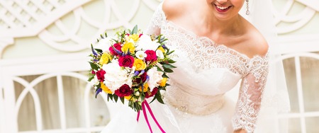 beautiful bouquet of different colors in the hands of the bride in a white dressの写真素材